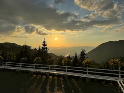 Sun setting over layered ridges from a rail-lined terrace of potted flowers