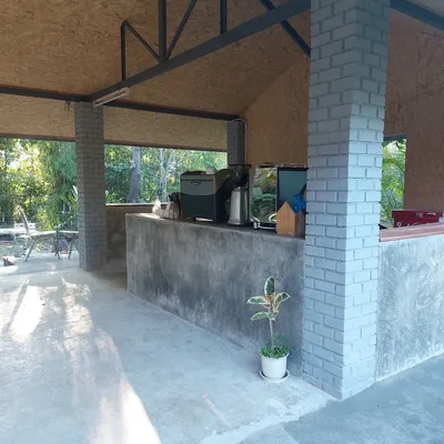 Bare concrete coffee counter with a grinder and espresso machine under an open timber roof