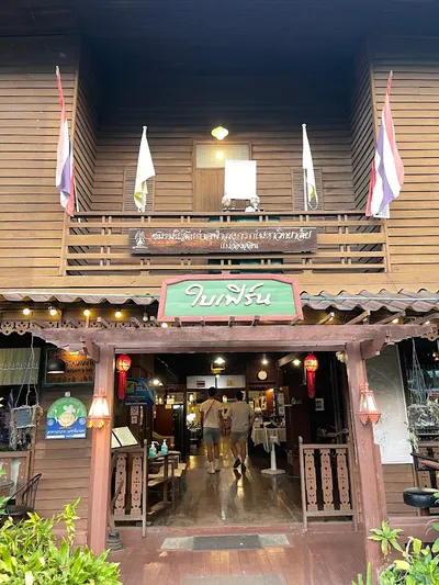 Teak restaurant entrance under Thai flags with a green Bai Fern sign
