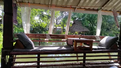 Bamboo sala with cushions and curtains looking across a farm pond