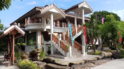 White and teak Lanna house with twin staircases above a rock garden