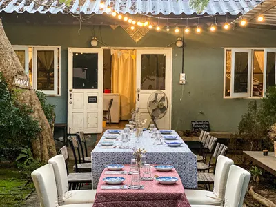 Long table laid for dinner in a garden courtyard under festoon lights