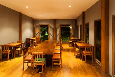 Warm-lit teak dining room with a long shared table and doors open to the garden