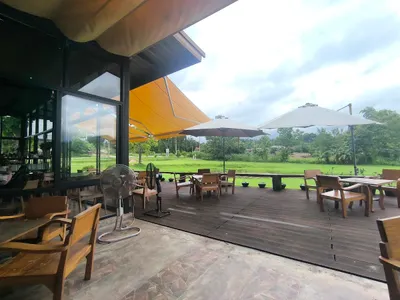 Teak chairs and parasols on a covered deck looking across a lawn to open fields