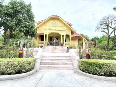 Yellow teak palace with shuttered windows behind a bronze statue and stone steps