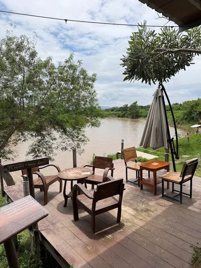Wooden chairs and a furled parasol on a deck above a wide brown river