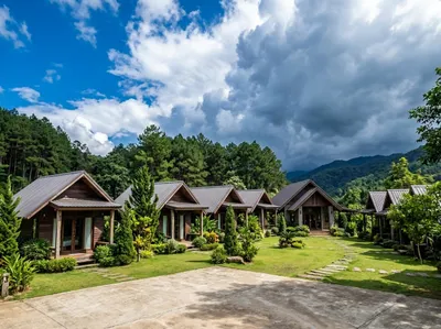 Row of dark timber bungalows with metal roofs and small porches around a lawn, forested hills behind