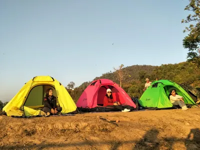 Three tents on a bare ridge at first light with people sitting in the doorways