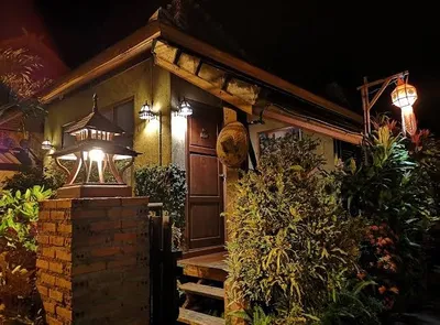 Lamplit guesthouse porch with a lantern post and dense planting at night