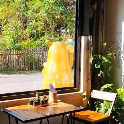 Window table with cactus pots and a yellow deer figure holding an ice cream outside