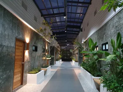 Planted corridor between guest room doors under a glazed roof at dusk