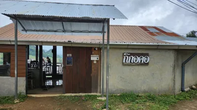 Tin-roofed village house with a painted Kikokor sign and shoes left at the open door