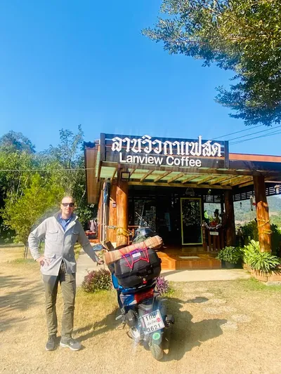Rider standing beside a loaded scooter outside the timber Lanview Coffee building