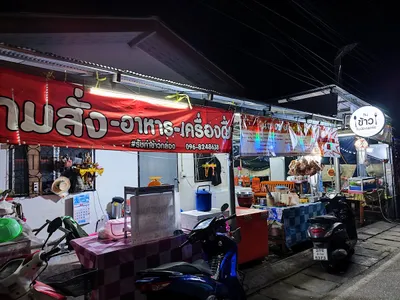 Night food stall under a red banner with scooters parked at the kerb