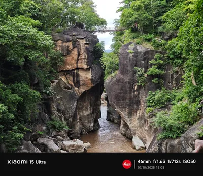 Muddy river squeezing between rock walls with a footbridge across the gorge