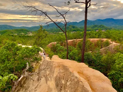 Walkers on a narrow sandstone ridge above forested hills at sunset