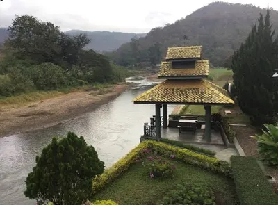 Tiered yellow-roofed sala on a lawn above the river with hills behind