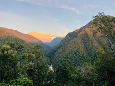 Forested ridges dropping to a river far below with cloud lit at sunset