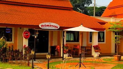 Orange-roofed Primavera pizzeria with a parasol and chairs on the front lawn