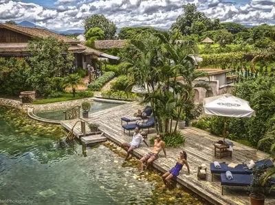 Guests on a timber deck beside a natural pool with palms and the resort behind