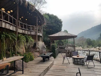 Thatched cafe terrace and a timber sala on the deck above a boulder-strewn river