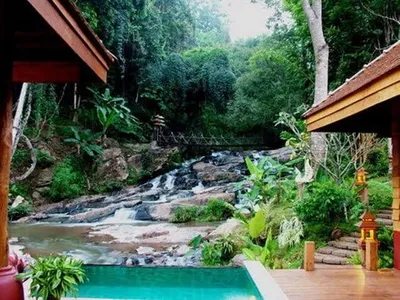 Pool and timber pavilions beside a rocky cascade with a suspension bridge above