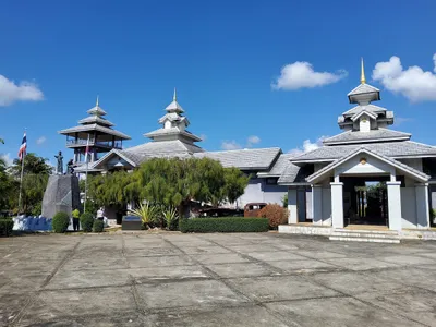 White tiered-roof memorial buildings and a statue across a concrete forecourt