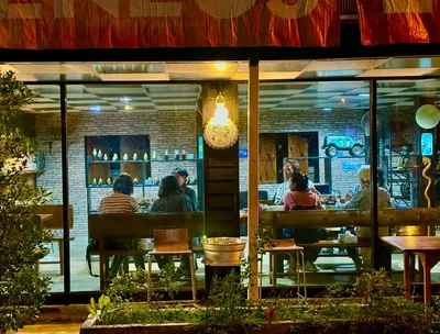 Diners at long tables inside a glass-fronted cafe lit at night