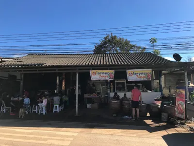 Roadside grill shop with clay rotisserie jars out front and families eating at plastic tables